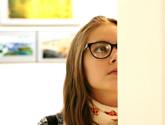 vhs Ausstellung & Vernissage: Lieblingswerke – Kunst, die erzählt Frau (Gesicht halb zu sehen, mit Brille) steht in einer Ausstellung und betrachtet etwas.
