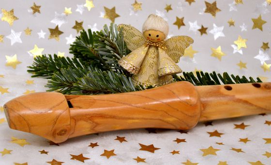 Winterliche Märchen mit Blockflötenspiel  Ein Sopran-Blockflöte liegt auf einem weißen Untergrund mit goldenen und silbernen Sternen. Hinter ihrsteht ein kleiner goldener Engel umgeben von Tannenzweigen.
