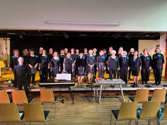 Foto des Chors auf einer Bühne, davor Instrumente und Stuhlreihen