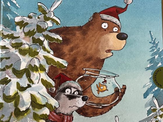 Ein Bär und ein Waschbär mit Weihnachtsmannmützen schauen hinter einem verschneiten Tannenbaum hervor. Der Bär trägt ein Glas mit Goldfisch.