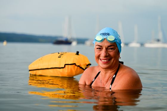 Eine Frau mit blauer Badekappe und hochgeschobener Schwimmbrille sitzt im Wasser, neben sich eine Schwimmboje.