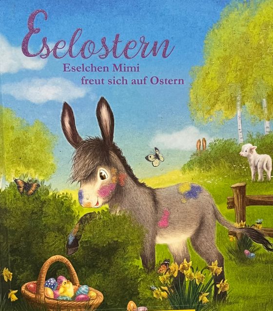 Ein kleiner Esel steht auf einer Frühlingswiese vor einem Strauch, hinter dem ein Korb mit Ostereiern versteckt ist.
