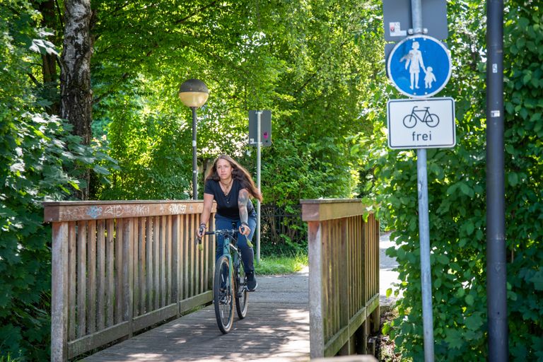 Mitarbeiterin der Gemeindeverwaltung fährt mit dem Fahrrad über eine Holzbrücke, die über den Gröbenbach führt