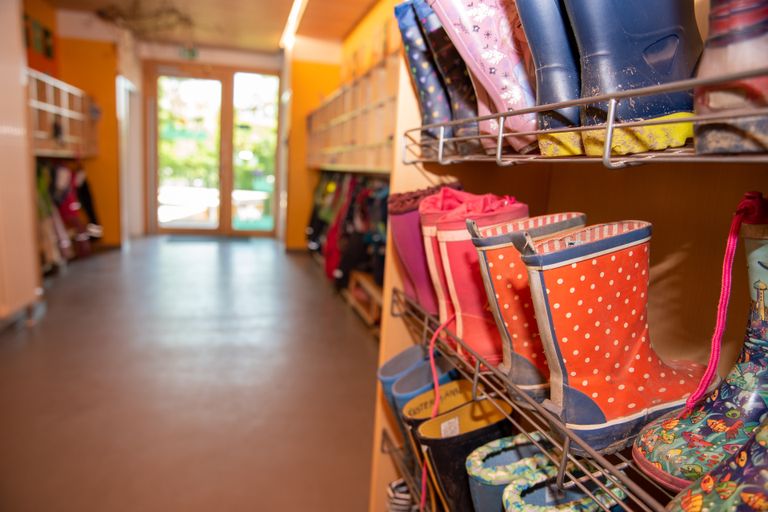 Gummistiefel stehen in einem Kindergarten im Schuhregal. Im Hintergrund sind Garderoben zu sehen.