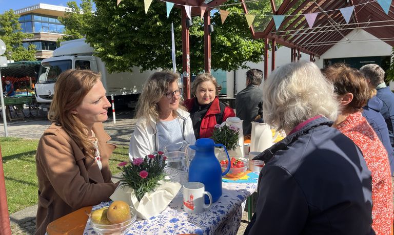 Damen und Herren sitzen an einem schön gedeckten Biertisch im der Sonne und unterhalten sich