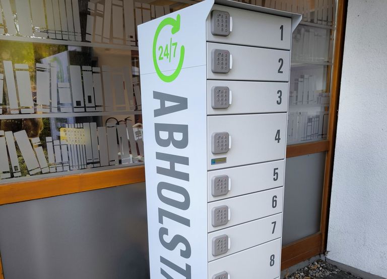 Bild der Station (weiß, 12 Fächer) vor dem Eingang der Bücherei. Nahaufnahme.