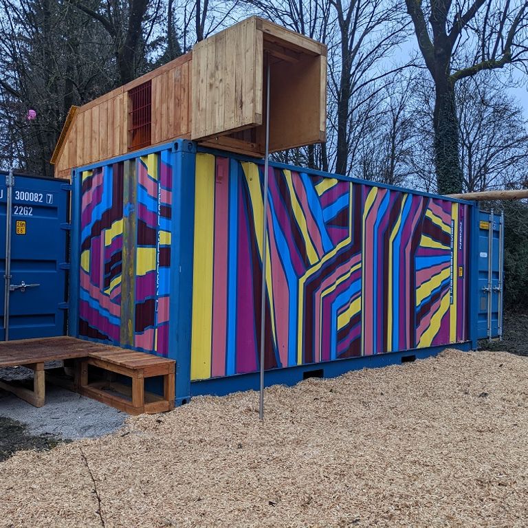 Rückansicht des Spielcontainers | © Gemeinde Gröbenzell Außenansicht des Spielcontainers von der Rückseite: Bunt bemalter Schiffscontainer mit Holzaufbau, Rutschstange und integrierter Schaukel